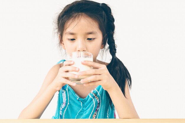 La ragazza asiatica sta bevendo un bicchiere di latte sopra fondo bianco