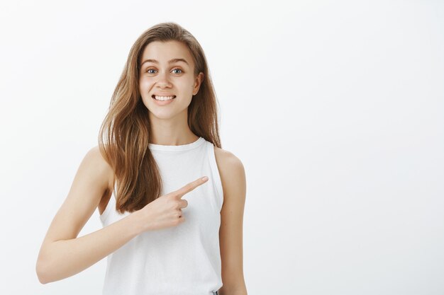 La ragazza attraente amichevole sorridente che indica a destra, dimostra il banner promozionale