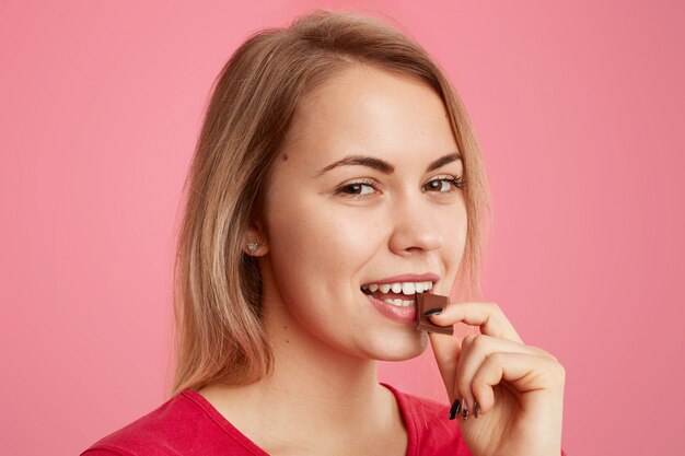 La ragazza attraente mangia un delizioso dessert, gode del cioccolato dolce, ha un trucco minimo