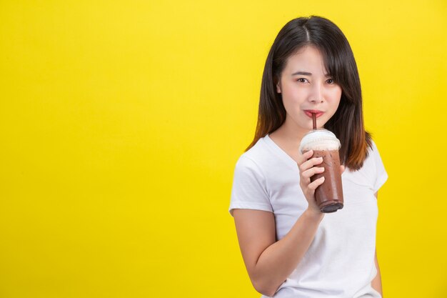 La ragazza beve acqua fredda dal cacao da un bicchiere di plastica trasparente su un giallo.