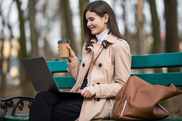 La ragazza beve il caffè e ha una videocall sul suo computer portatile all'esterno