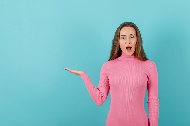 La ragazza bionda sorpresa sta indicando a sinistra con la mano su fondo blu