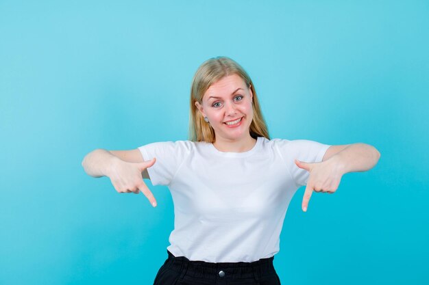 La ragazza bionda sorridente sta puntando verso il basso con gli indici su sfondo blu