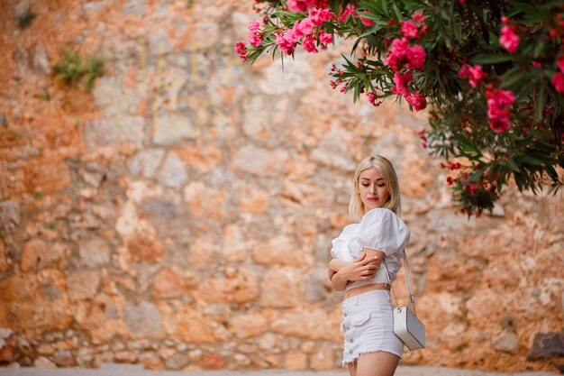 La ragazza bionda sta guardando in basso incrociando le braccia su uno sfondo di pietra