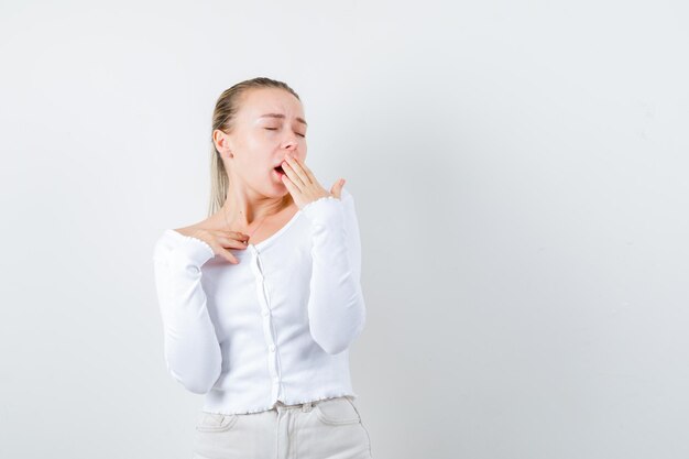 La ragazza bionda sta sbadigliando su sfondo bianco