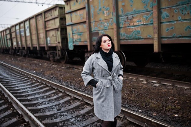 La ragazza castana in cappotto grigio ha posato nella stazione ferroviaria