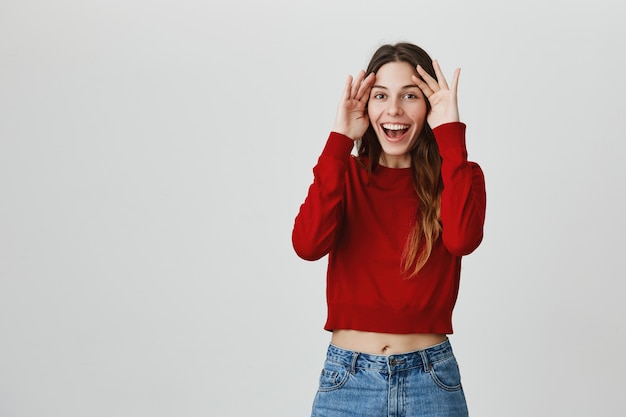 La ragazza castana sorridente allegra si tiene per mano sul fronte, fa il gesto di peekaboo