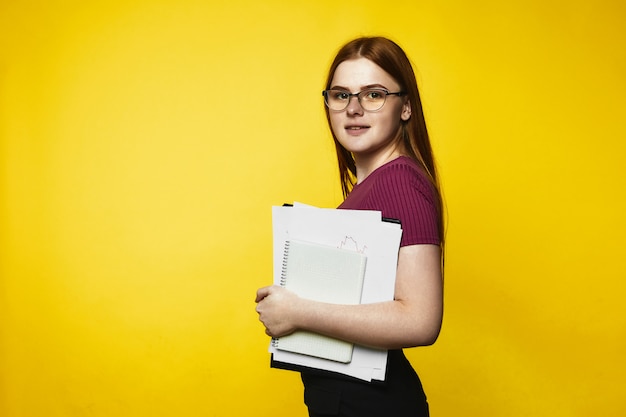 La ragazza caucasica sorrisa della testarossa sta tenendo i taccuini e gli archivi in mani