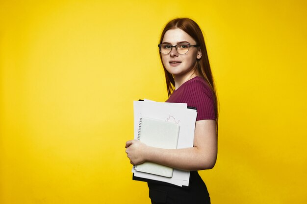 La ragazza caucasica sorrisa della testarossa sta tenendo i taccuini e gli archivi in mani