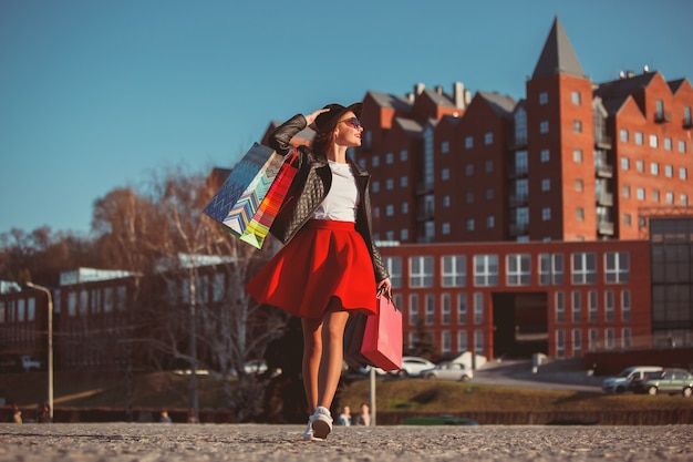 La ragazza che cammina con i sacchetti della spesa sulle vie della città al giorno soleggiato
