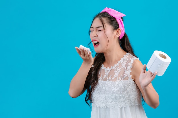 La ragazza che indossa un pigiama bianco non è a suo agio. Usando dei fazzoletti per asciugarsi il naso su un blu.