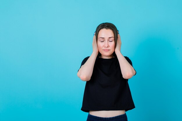 La ragazza con gli occhi chiusi sta coprendo le orecchie con le mani su sfondo blu