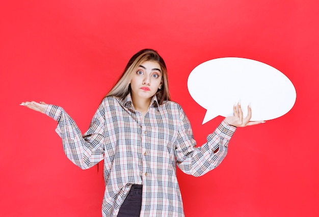 La ragazza con un maglione a quadri che tiene in mano un'ideaboard ovale sembra inesperta e persa