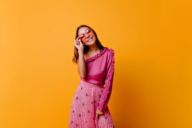 La ragazza con un sorriso abbagliante in uno stato d'animo carino posa per foto in un ambiente caldo e luminoso Modello in abito elegante mette gli occhiali