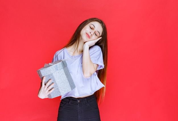 La ragazza con una confezione regalo d'argento sembra stanca e assonnata.