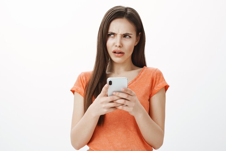 Foto gratuito la ragazza confusa e insicura che guarda nell'angolo in alto a sinistra perplessa durante l'utilizzo del telefono cellulare, non riesce a capire qualcosa