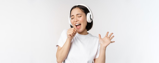 La ragazza coreana canta e ascolta la musica in cuffia divertendosi si erge su sfondo bianco
