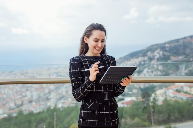 La ragazza del blogger del computer di Planshet sta sorridendo guardando lo schermo sullo sfondo della vista sulla città