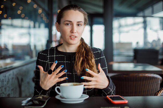 La ragazza del blogger sta parlando aprendo le mani nella caffetteria