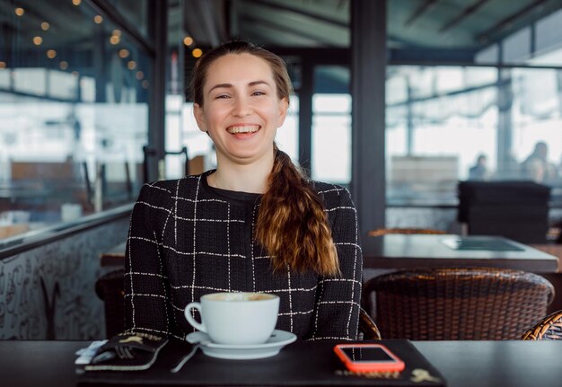 La ragazza del blogger sta ridendo guardando la fotocamera nella caffetteria