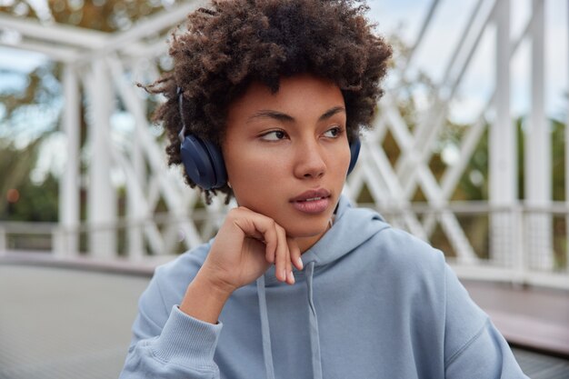 la ragazza distoglie lo sguardo essendo immersa nei pensieri ascolta la traccia audio tramite le cuffie vestita con una felpa con cappuccio pone all'esterno