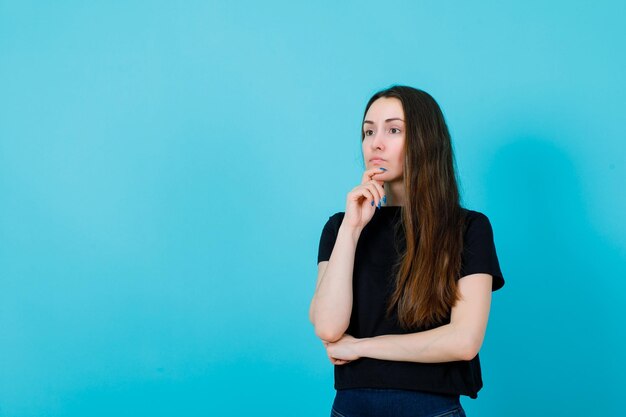 La ragazza distoglie lo sguardo sta pensando mettendo la mano sul mento su fondo blu