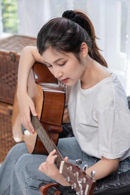 La ragazza è seduta e suona la chitarra sulla sedia.