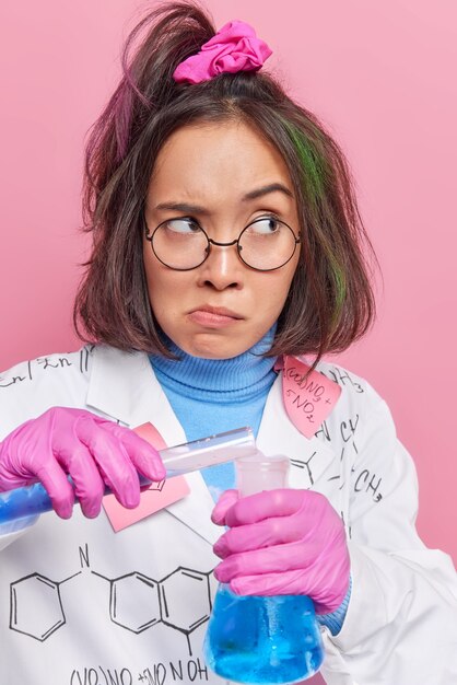 la ragazza fa ricerche con i fluidi chimici lavora in laboratorio con campioni liquidi indossa occhiali rotondi e posa medica su rosa