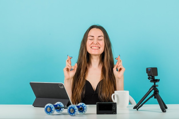 La ragazza felice del blogger sta chiudendo gli occhi incrociando le dita su sfondo blu