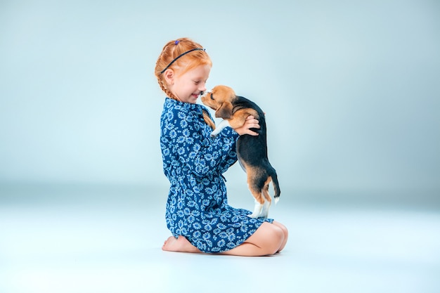 La ragazza felice e un cucciolo di beagle sul muro grigio