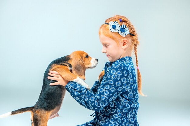 La ragazza felice e un cucciolo di beagle sulla parete grigia