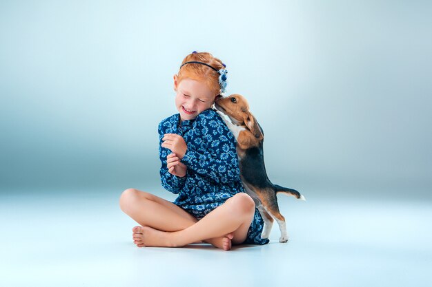 La ragazza felice e un cucciolo di beagle sulla parete grigia