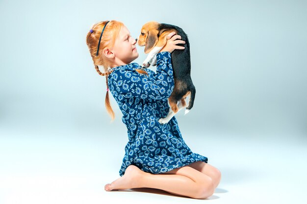 La ragazza felice e un cucciolo di beagle sulla parete grigia