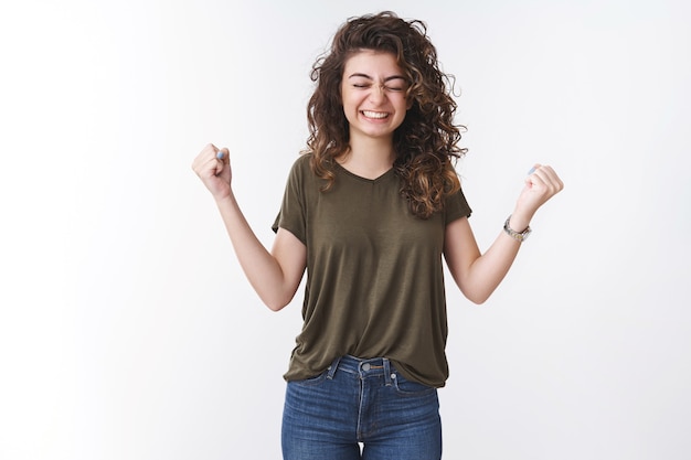 La ragazza felice ha realizzato il sogno stringere con gioia i pugni celebrando la vittoria sorridendo dire di sì chiudere gli occhi felicemente raggiungere l'obiettivo realizzare ricevere buone notizie positive, trionfante sfondo bianco