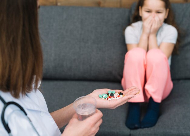 La ragazza ha paura della sua dottoressa dando medicine e bicchiere d&#39;acqua in mano