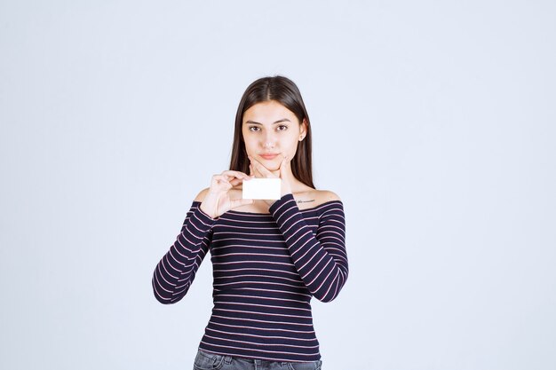 La ragazza in camicia a righe tiene un biglietto da visita e sembra pensierosa.