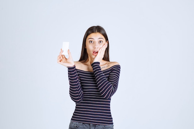 La ragazza in camicia a righe tiene un biglietto da visita e sembra sorpresa.