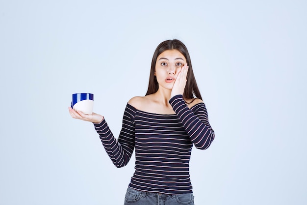 La ragazza in camicia a righe tiene una tazza di caffè e sembra confusa.