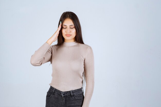 La ragazza in camicia grigia ha mal di testa o stanca.