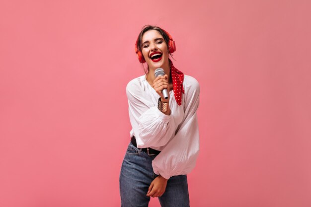 La ragazza in cuffia tiene il microfono e canta la sua canzone preferita. Giovane donna in abiti alla moda con rossetto luminoso in posa.