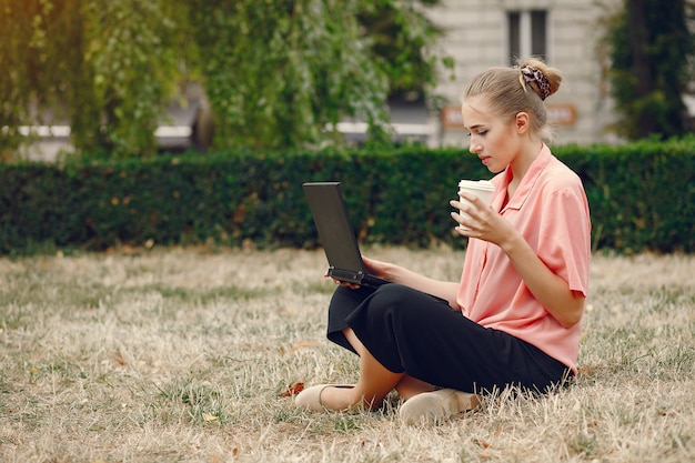 La ragazza in una camicia rosa che si siede in un parcheggio e usa il computer portatile