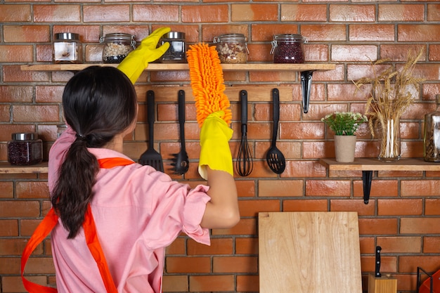 La ragazza indossa guanti gialli mentre pulisce la stanza del kichen con spolverino nella sua casa.