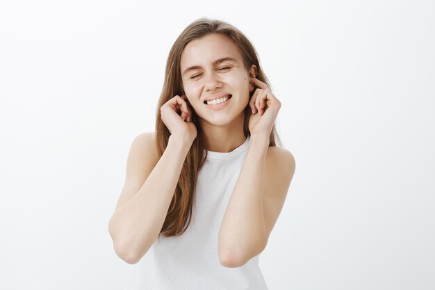 La ragazza infantile sorridente allegra ignora la persona, chiude le orecchie con le dita