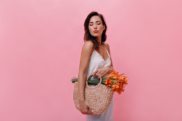 La ragazza manda un bacio e una borsa con fiori su sfondo rosa