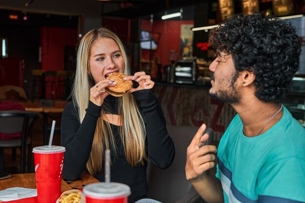 La ragazza morde l'hamburger in caffè con il suo ragazzo.