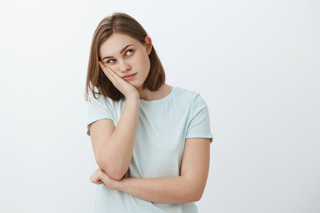 La ragazza pensa che la festa sia zoppa. Annoiato giovane femmina europea con corto taglio di capelli castano appoggiato la testa sul palmo che guarda nell'angolo in alto a destra pensando usando l'immaginazione per intrattenere se stessa mentre muore di noia