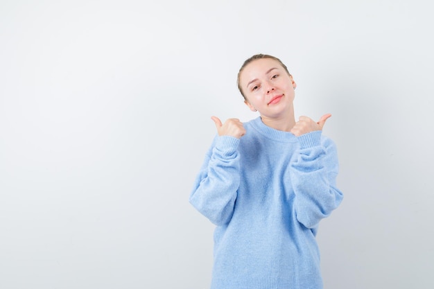 La ragazza piacevole sta mostrando i suoi pollici su fondo bianco