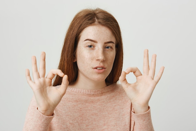 La ragazza rossa attraente sicura mostra il gesto giusto, assicura nessun problema, tutto bene