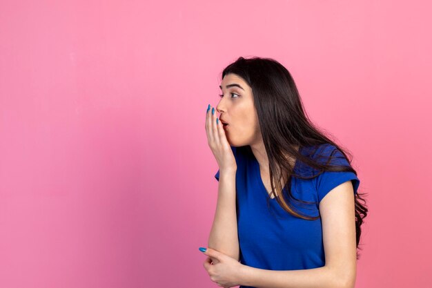 La ragazza scioccata chiuse la bocca con la mano e guardando da parte su sfondo rosa Foto di alta qualità