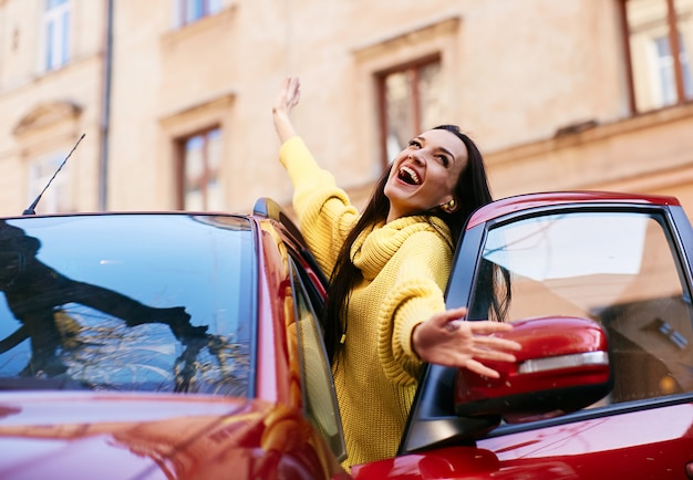 La ragazza si rallegra nella vita e siede nella sua macchina rossa